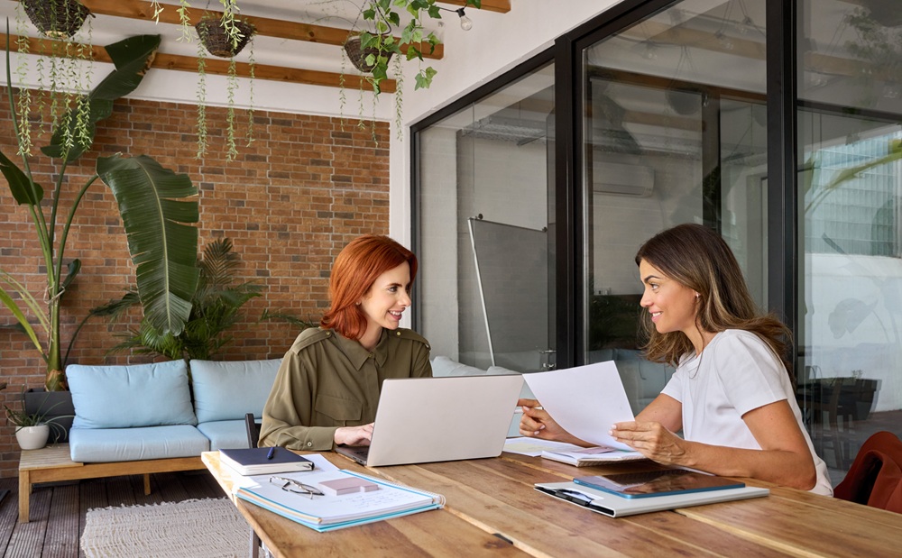 Collaborative Business Planning Session – Dentist Advisor Group Two professional women discussing business documents and strategies in a modern office setting, representing expert collaboration and advisory support – Dentist Advisor Group